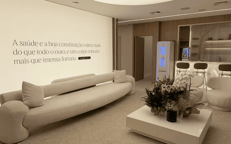 Lounge do Instituto Evollution: sofá curvo claro, poltronas e uma frase sobre saúde pintada na parede